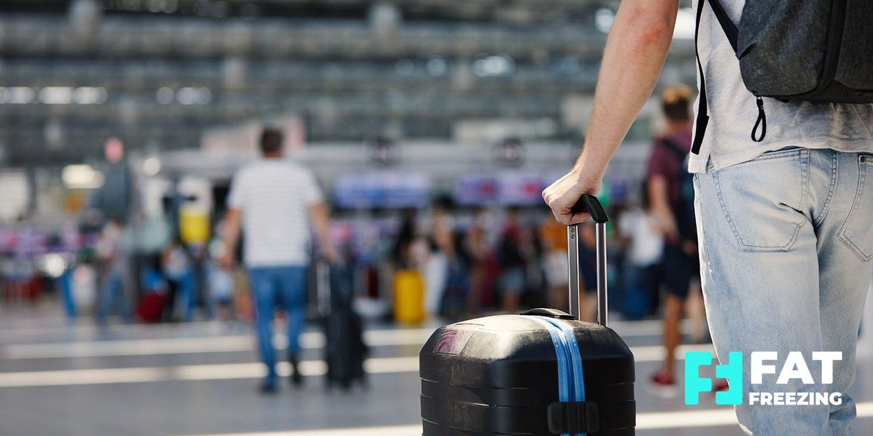 Man walking through an airport check-in hall pulling a wheeled suitcase
