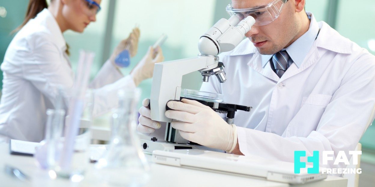 Researcher looking into a microscope in a laboratory with a colleague working behind